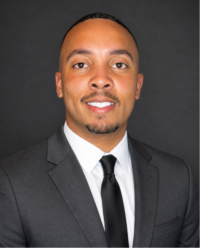 Man wearing a gray suit and black tie against a dark background